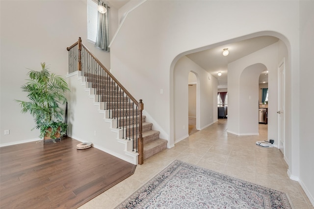 entrance foyer with plenty of natural light, arched walkways, light wood-style floors, a high ceiling, and baseboards