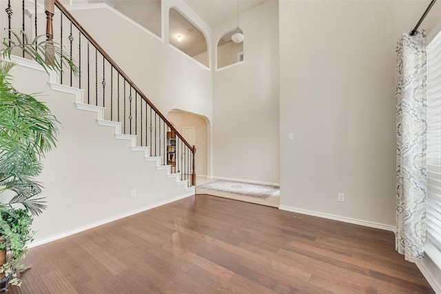 foyer entrance featuring arched walkways, dark wood-style floors, stairway, and a towering ceiling