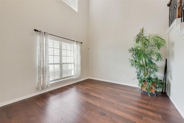 unfurnished room featuring wood finished floors, baseboards, and a towering ceiling