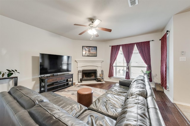 living room featuring visible vents, a fireplace with raised hearth, a ceiling fan, and wood finished floors