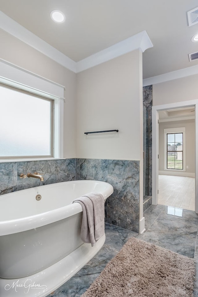 full bathroom with a freestanding tub, a wainscoted wall, visible vents, marble finish floor, and tile walls