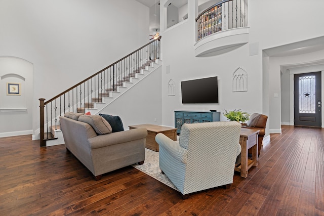 living area with a high ceiling, dark wood-type flooring, stairway, and baseboards