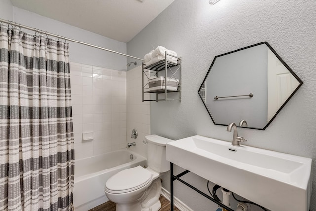 bathroom featuring wood finished floors, shower / bathtub combination with curtain, a sink, toilet, and a textured wall