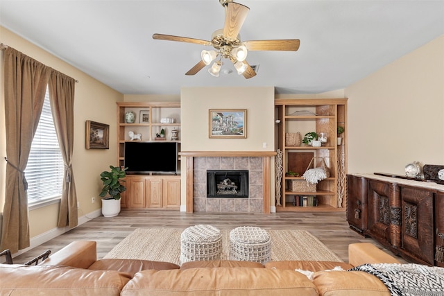 living room with a ceiling fan, a fireplace, baseboards, and light wood finished floors