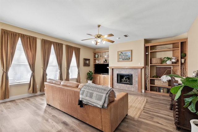 living area featuring wood finished floors, baseboards, visible vents, a fireplace, and ceiling fan