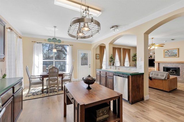 dining room with a tiled fireplace, light wood-style floors, arched walkways, and baseboards