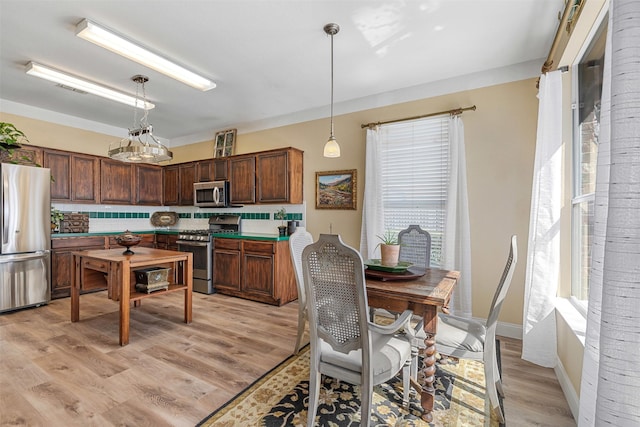 kitchen featuring decorative light fixtures, stainless steel appliances, light wood-style floors, and decorative backsplash