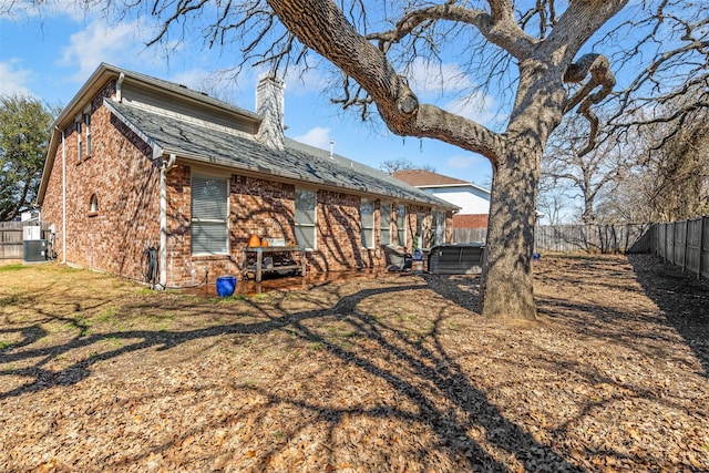 rear view of house featuring brick siding, a fenced backyard, and a chimney