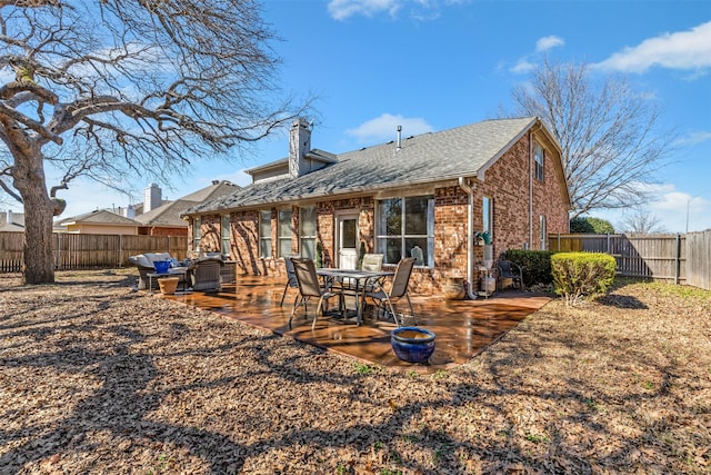 rear view of house with brick siding, a patio, a chimney, and a fenced backyard