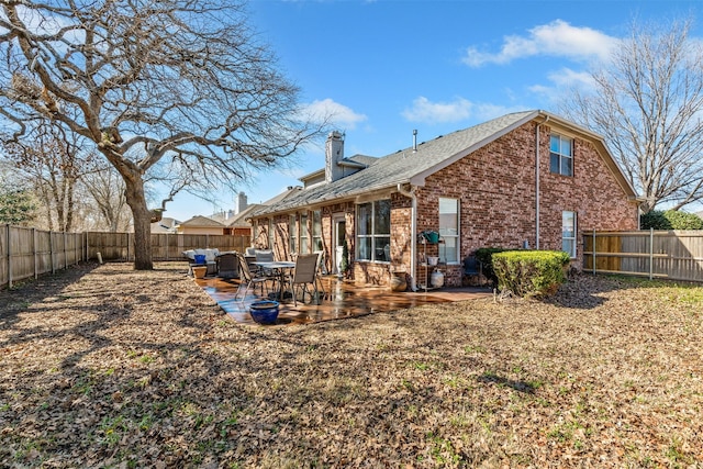 back of property with brick siding, a patio area, a chimney, and a fenced backyard