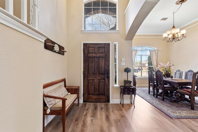 entryway featuring wood finished floors, baseboards, visible vents, ornamental molding, and a chandelier