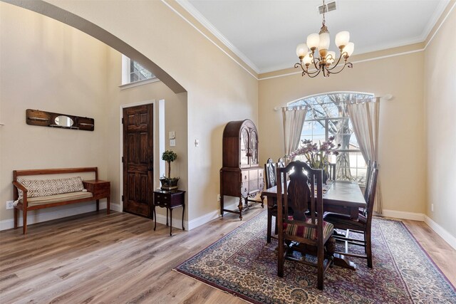 dining space with visible vents, crown molding, light wood-style floors, arched walkways, and a notable chandelier