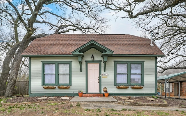 view of front facade featuring a carport, a shingled roof, and fence