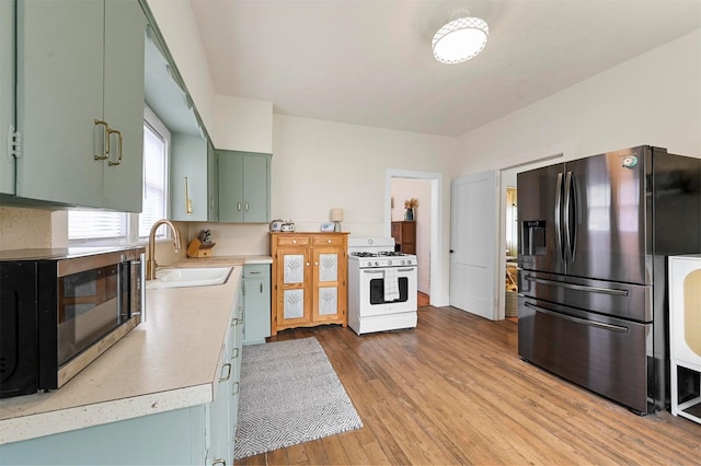 kitchen featuring green cabinets, light countertops, appliances with stainless steel finishes, light wood-style floors, and a sink