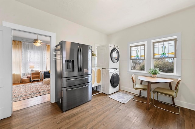 kitchen featuring hardwood / wood-style flooring, stainless steel fridge with ice dispenser, stacked washer and clothes dryer, and baseboards