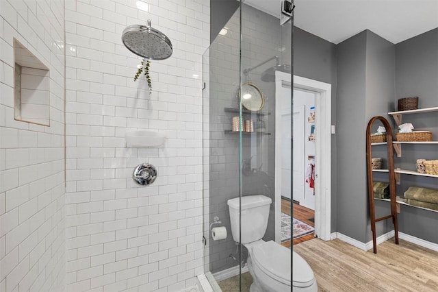 full bath featuring baseboards, toilet, wood finished floors, and a shower stall