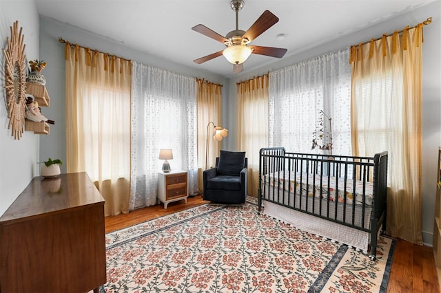 bedroom with a ceiling fan, a nursery area, and wood finished floors