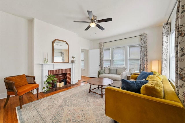 living area with ceiling fan, baseboards, a brick fireplace, and wood finished floors