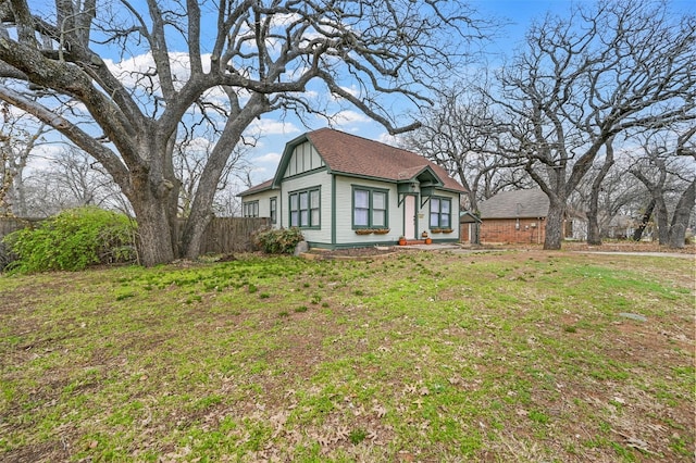 tudor house with a front yard, fence, and a shingled roof