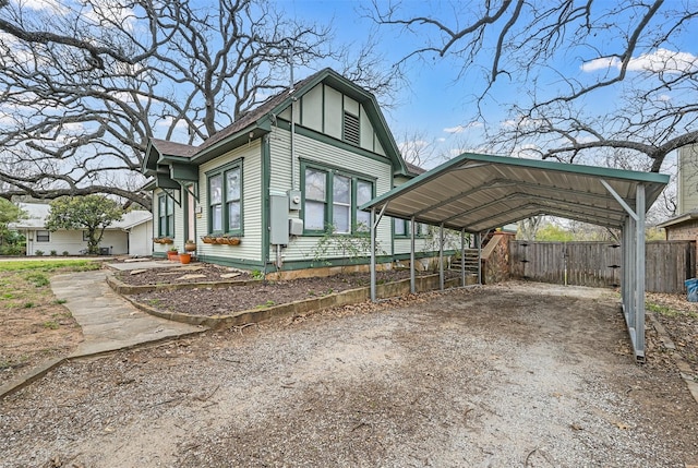 view of front facade with a carport, roof with shingles, dirt driveway, and fence