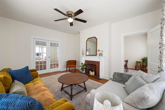 living area with baseboards, french doors, a fireplace, wood finished floors, and a ceiling fan