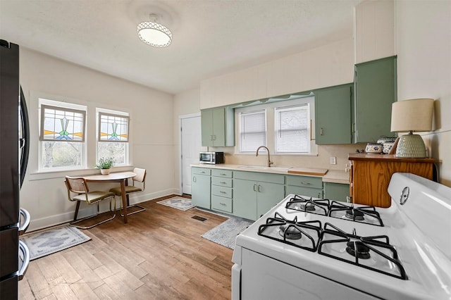 kitchen with green cabinetry, freestanding refrigerator, a sink, light countertops, and white gas range oven