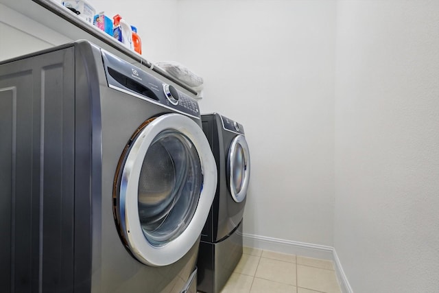 washroom featuring light tile patterned flooring, laundry area, washer and clothes dryer, and baseboards