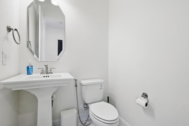 half bath featuring toilet, baseboards, and a sink