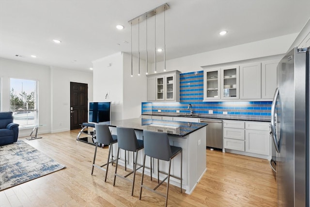 kitchen featuring light wood-type flooring, a kitchen bar, a sink, backsplash, and stainless steel appliances