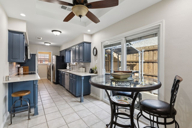 kitchen with a tray ceiling, blue cabinetry, a sink, stainless steel appliances, and light countertops