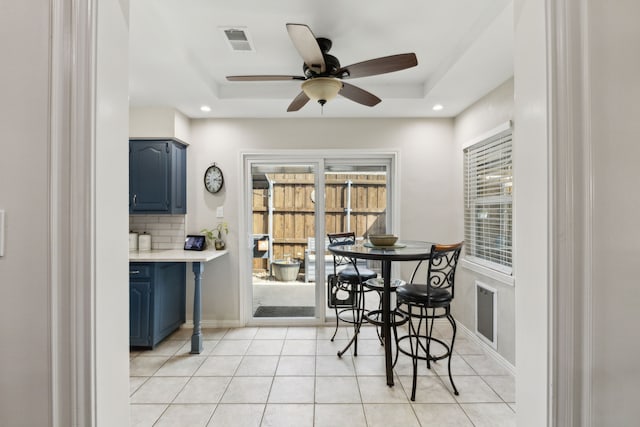 dining space with a tray ceiling, light tile patterned floors, a ceiling fan, and visible vents