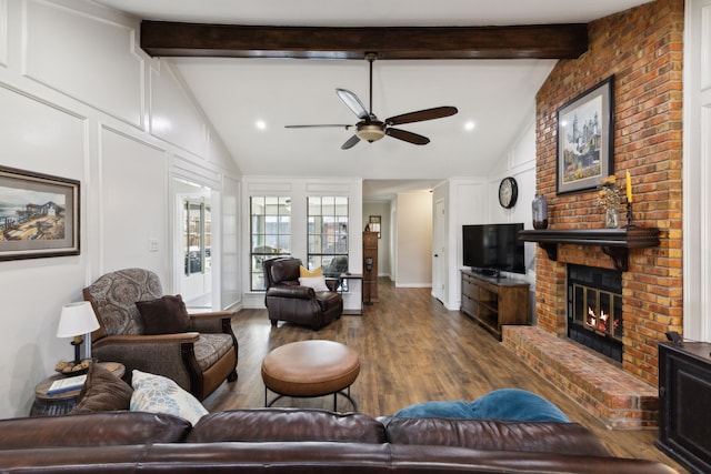 living room featuring a ceiling fan, lofted ceiling with beams, wood finished floors, a decorative wall, and a brick fireplace