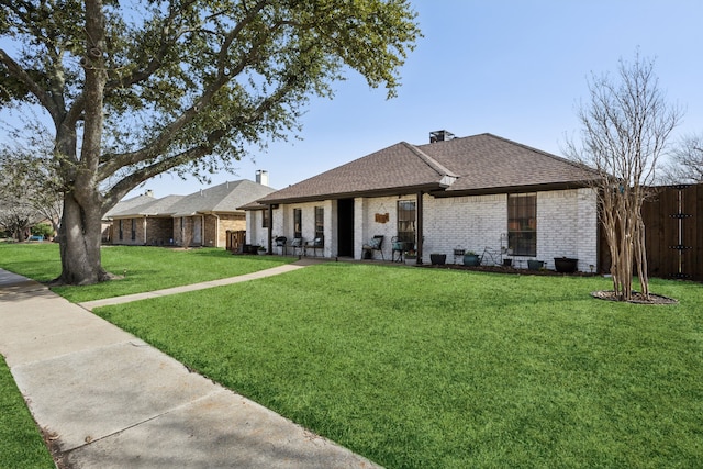 ranch-style home with a front yard, fence, brick siding, and a shingled roof