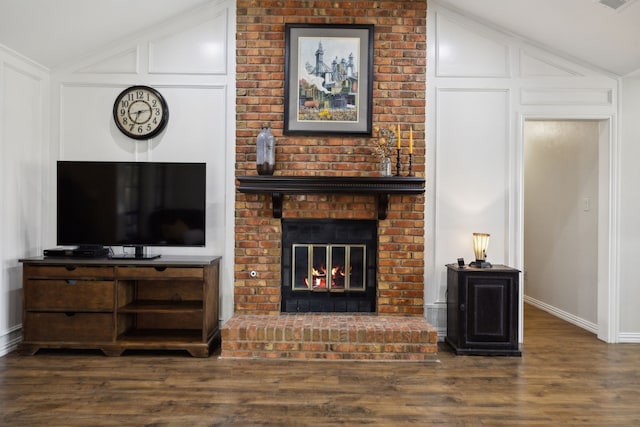 living room with visible vents, vaulted ceiling, a fireplace, wood finished floors, and a decorative wall