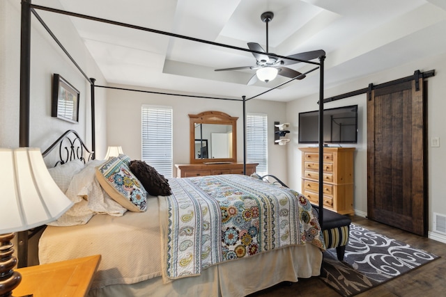 bedroom with visible vents, a tray ceiling, wood finished floors, a barn door, and ceiling fan