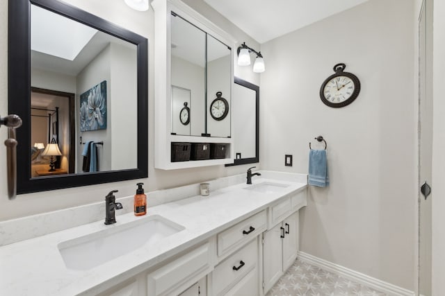 full bath featuring double vanity, a skylight, baseboards, and a sink