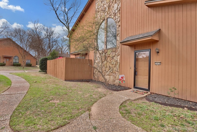 view of home's exterior with a yard, stone siding, and fence