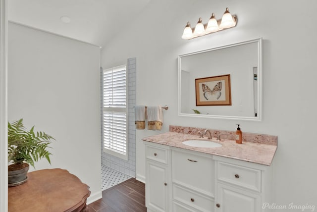 bathroom featuring vanity, a shower, lofted ceiling, and wood finished floors