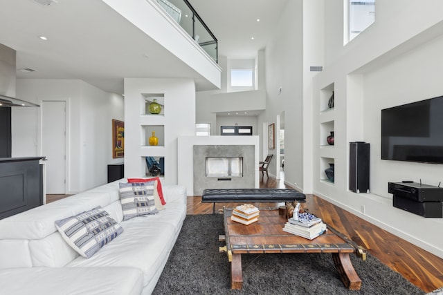 living room with built in features, wood finished floors, a high ceiling, a fireplace, and baseboards