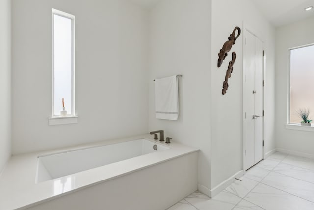 full bathroom featuring a garden tub, baseboards, and marble finish floor