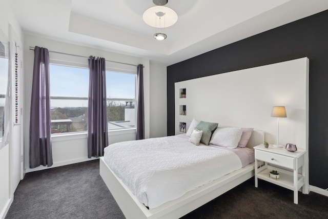 bedroom with baseboards, a tray ceiling, and dark colored carpet