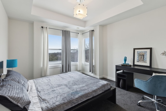 carpeted bedroom featuring a tray ceiling and baseboards