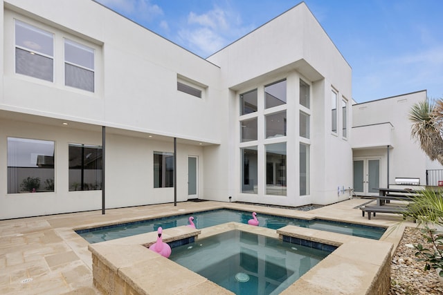 back of property with stucco siding, french doors, a pool with connected hot tub, and a patio