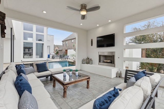 living room featuring recessed lighting, a ceiling fan, and an outdoor fireplace