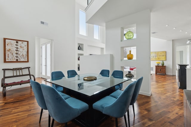 dining area featuring built in shelves, dark wood-style floors, visible vents, baseboards, and a high ceiling