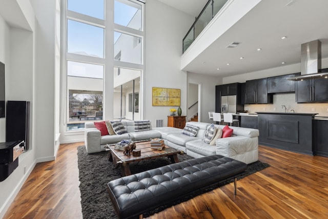 living room featuring stairway, wood finished floors, visible vents, and a towering ceiling