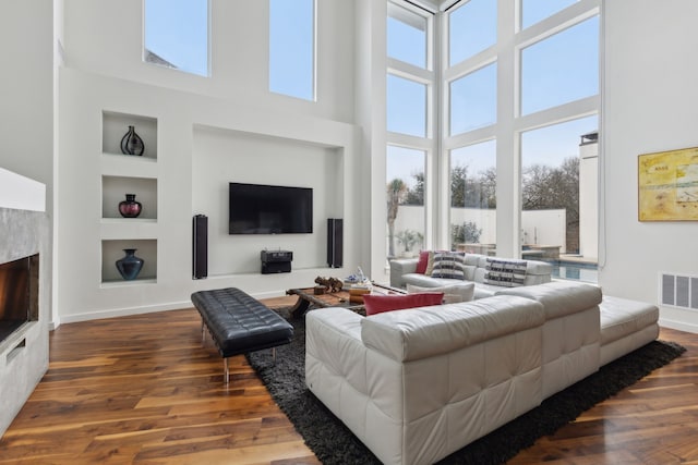 living area featuring built in shelves, baseboards, a lit fireplace, and wood finished floors