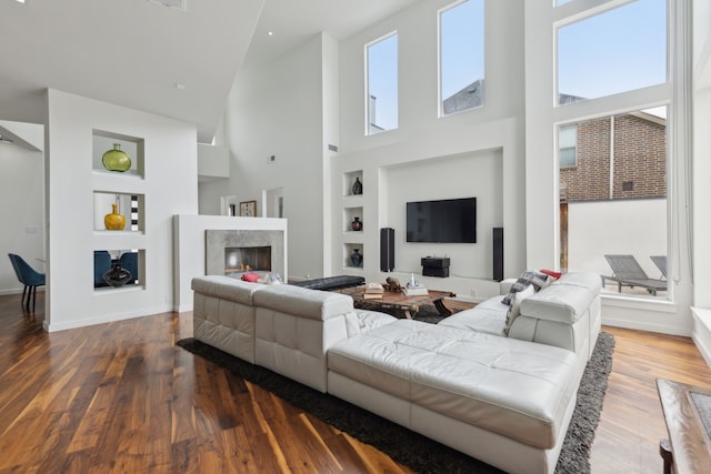 living room featuring built in features, baseboards, wood finished floors, and a high end fireplace