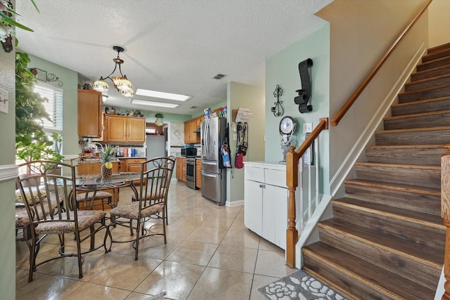 dining room with visible vents, stairs, light tile patterned floors, a skylight, and a textured ceiling