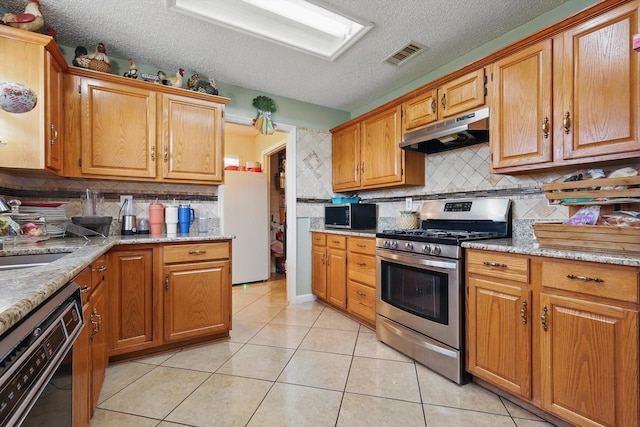 kitchen featuring visible vents, under cabinet range hood, appliances with stainless steel finishes, light tile patterned flooring, and a sink